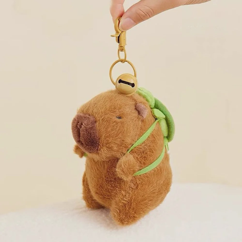 Bag charm of brown capybara plush wearing a green bag pack with bell attached