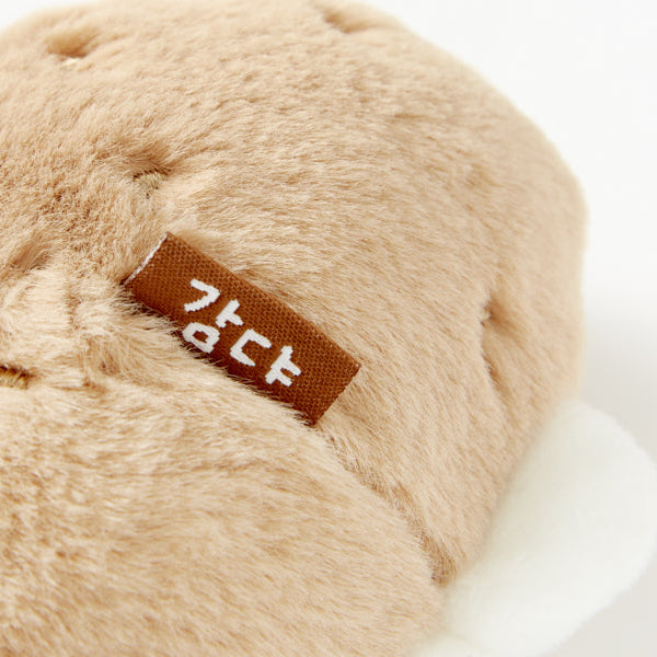 Beige plush toy with a brown label on a white background