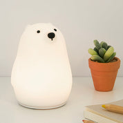 White bear-shaped night light on a white surface with a small potted plant and notebook.