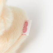 Close-up of a fluffy white bag charm with a brand tag on a light background