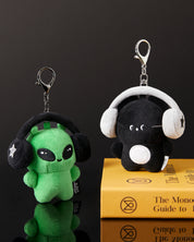 Two plush keychains with alien designs wearing headphones on a black background.