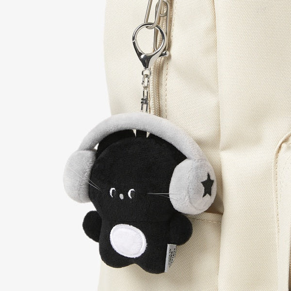 Plush keychain with a black cat wearing headphones attached to a beige backpack.