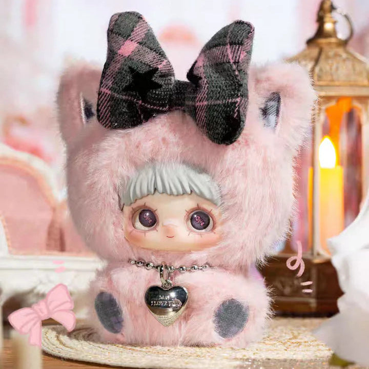 Toy figure with pink fur and plaid bow, 'First Love' text on a blurred background