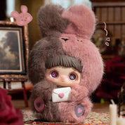 Plush toy with rabbit ears and a letter, set against a blurred indoor background.