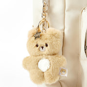 Teddy bear keychain with a star charm attached to a beige bag.