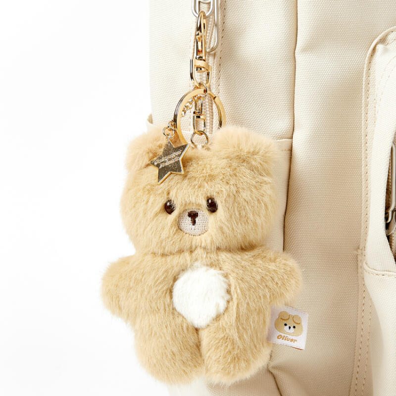 Teddy bear keychain with a star charm attached to a beige bag.