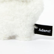 White fluffy keychain with a black 'Adore!' tag on a white background