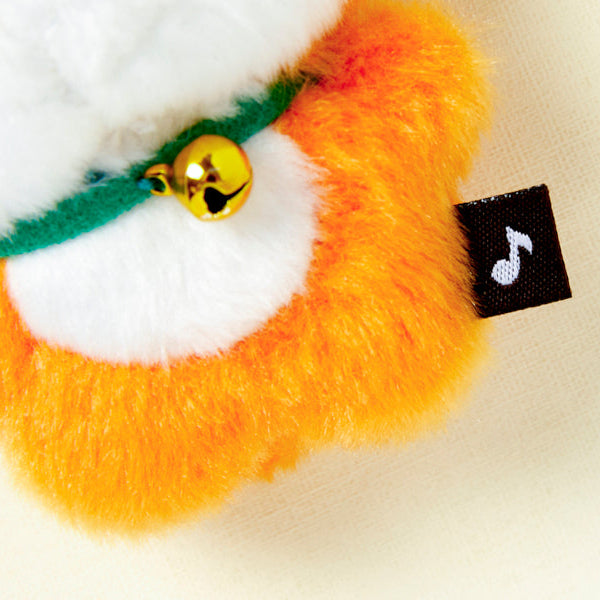 Close-up of a plush toy with a gold bell and music note tag on a white background