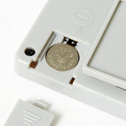 Close-up of a white electronic device with a coin inserted, on a light gray background.