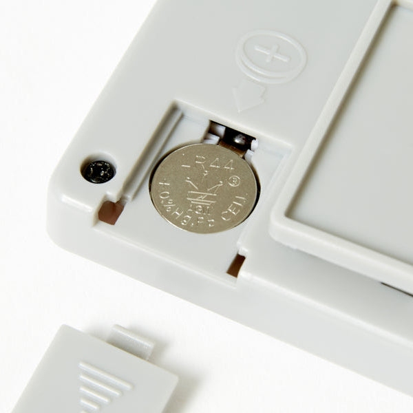 Close-up of a white electronic device with a coin inserted, on a light gray background.
